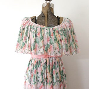 May include: A pink and green floral print dress with a ruffled neckline and a pink sash. The dress is made of a lightweight, pleated fabric.