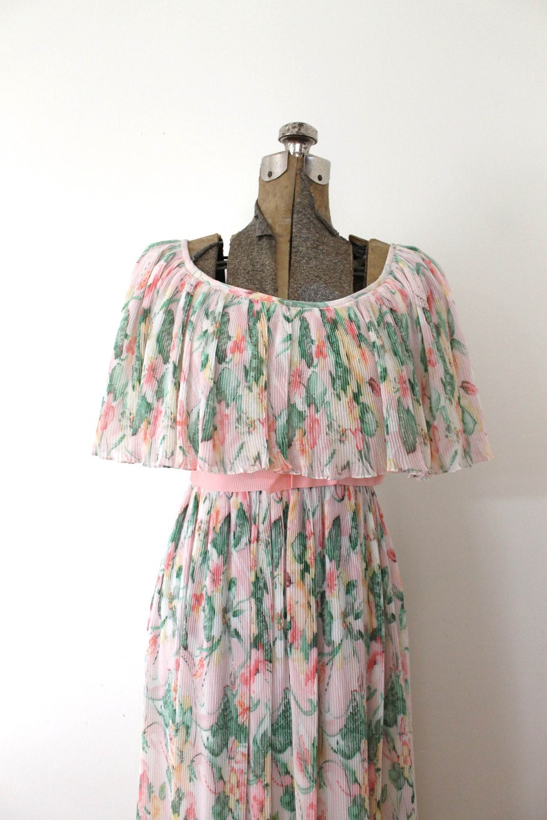 May include: A pink and green floral print dress with a ruffled neckline and a pink sash. The dress is made of a lightweight, pleated fabric.