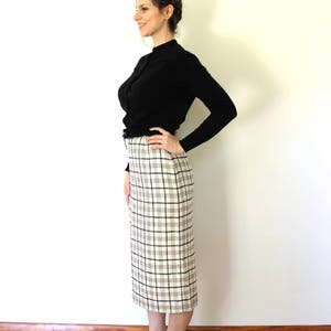 May include: A woman wearing a black mock neck shirt and a white and black plaid skirt. She is wearing black heels and has her hair pulled back in a braid.