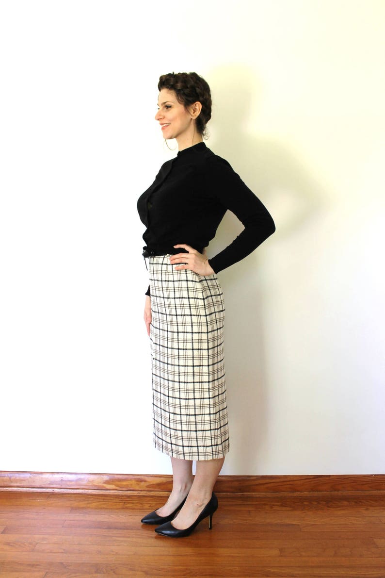 May include: A woman wearing a black mock neck shirt and a white and black plaid skirt. She is wearing black heels and has her hair pulled back in a braid.