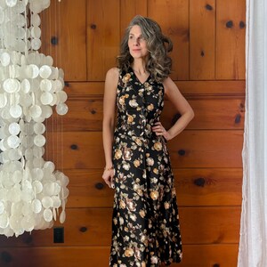 K&ouml;nnte beinhalten: Eine Frau tr&auml;gt ein schwarzes Midikleid mit Blumenmuster und braunen Schuhen mit Absatz. Das Kleid hat einen V-Ausschnitt und eine Knopfleiste vorne.