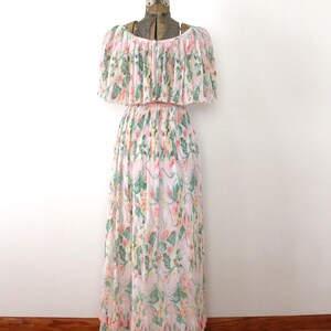 May include: A white maxi dress with a pink floral print and a ruffled neckline. The dress has a tiered skirt and is made of a lightweight fabric.