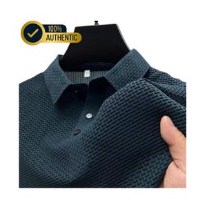 May include: Dark teal polo shirt with a textured weave pattern. The shirt has a classic collar and two buttons. The image includes a gold and black badge that says "100% AUTHENTIC".