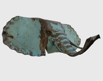 May include: A metal elephant head sculpture with a distressed, aged appearance. The sculpture features a turquoise and brown color palette, with visible wear and tear. The elephant's trunk is extended, and the ears are large and detailed.