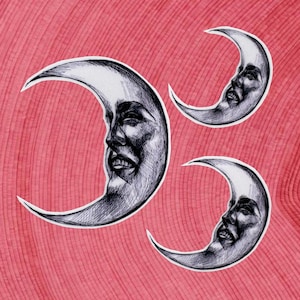 Può includere: Tre adesivi a forma di luna crescente con volti umani, resi a inchiostro nero e bianco. Le lune sono ambientate su uno sfondo rosa-rossastro strutturato. I volti hanno tratti ed espressioni dettagliate.