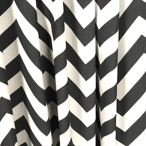 Può includere: Primo piano di un tessuto con un motivo a zig-zag bianco e nero. Il tessuto è drappeggiato, creando morbide pieghe e ombre. Il design audace e ripetitivo è visivamente sorprendente e moderno.