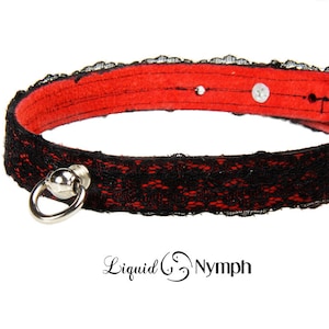 May include: Black lace choker with a red velvet backing and a silver metal ring with a ball accent. Liquid Nymph is printed below the choker.