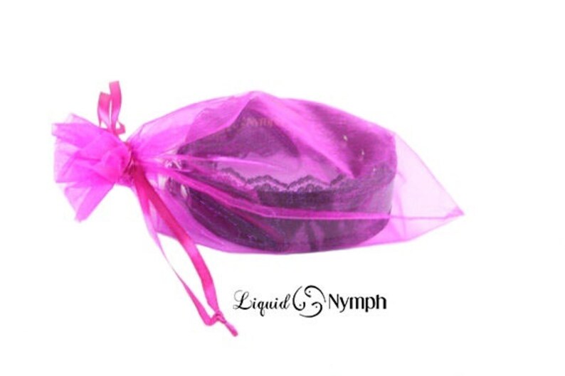 May include: A pink organza bag with a black lace trim, tied with a pink ribbon. The bag is filled with a black lace choker.