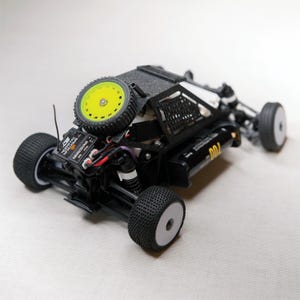 May include: A black and white remote control car with a spare yellow wheel. The car has a detailed chassis, black tires, and a small electronic component. The spare wheel is mounted on the back.