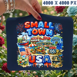 May include: Navy blue graphic tee featuring a colorful illustration of a small town scene. The design includes the text "SMALL TOWN USA", a diner, a post office, a boat, and the Route 66 sign. Fireworks and an American flag are also included.