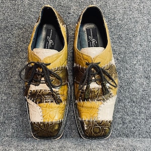 May include: A pair of lace-up shoes featuring a patchwork design with textured, crocodile-embossed leather panels in shades of olive green, mustard yellow, and cream. The shoes have black laces and a label reading Giorgio Brutini inside.