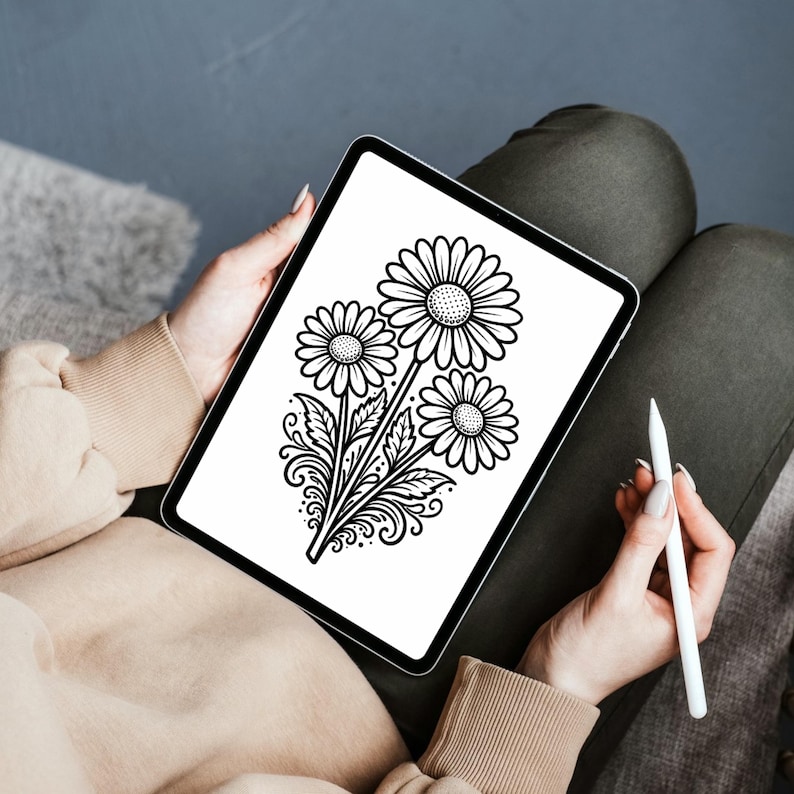以下が含まれることがあります： 3つのデイジーの花の白黒のイラストが表示されたデジタルタブレット。ベージュのセーターとオリーブグリーンのズボンを着た人がタブレットを持ち、白いスタイラスを持っています。
