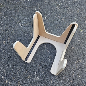 May include: A wooden guitar stand with a natural finish. The stand has a unique Y-shaped design with a curved base and black metal reinforcement strips. The stand is designed to hold a guitar.
