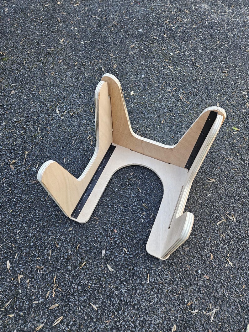 May include: A wooden guitar stand with a natural finish. The stand has a unique Y-shaped design with a curved base and black metal reinforcement strips. The stand is designed to hold a guitar.