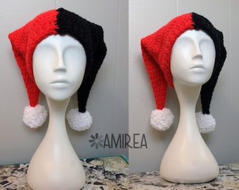 May include: A red and black crocheted hat with white pom-poms on the ends of the tails. The hat is on a white mannequin head.