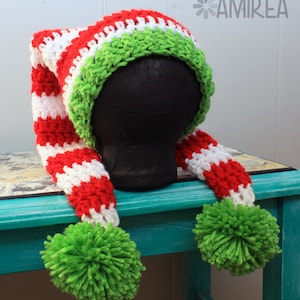 May include: A red and white striped crochet elf hat with green trim and pom-poms. The hat is on a mannequin head and the hat has long tails with pom-poms.