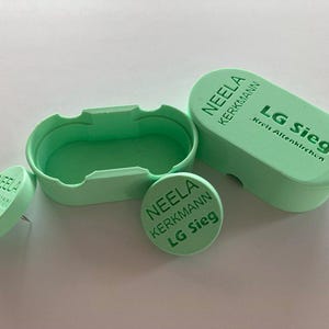 Könnte beinhalten: Drei grüne Plastikbehälter mit dem Text "NEELA KERKMANN LG Sieg Kreis Altenkirchen" darauf. Die Behälter dienen zur Aufbewahrung von Kleinteilen.