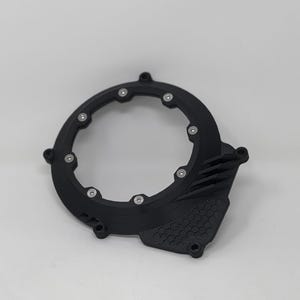 May include: Black circular mechanical component with silver fasteners. The part features a hexagonal pattern and parallel lines. Designed to fit around a circular object, it is likely a protective cover.