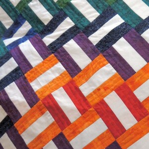 以下が含まれることがあります： 白、オレンジ、赤、紫、緑、青の正方形が織り込まれたキルトです。