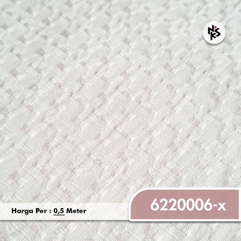 May include: White fabric with a textured, repeating square pattern. The fabric has a subtle, raised design. The number "6220006-x" is displayed on a pink label. The text "Harga Per : 0,5 Meter" is also visible.