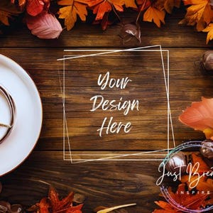 Könnte beinhalten: Ein rustikaler Holzgrund mit Herbstblättern in Orange-, Rot- und Brauntönen. Links im Bild befindet sich ein weißer Teller mit einem goldenen Ring. In der Mitte des Bildes befindet sich ein weißes Rechteck mit dem Text "Your Design Here". Der Text "Just Breathe Inspire" befindet sich in der unteren rechten Ecke des Bildes.