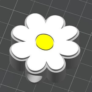 Op de afbeelding: Een 3D-geproduceerde madelief met witte bloemblaadjes en een gele kern. De bloem heeft een dikke, grijze omtrek, waardoor hij een verhoogde uitstraling heeft. De achtergrond is een donkergrijs raster, dat een contrasterende achtergrond vormt voor de heldere bloem.