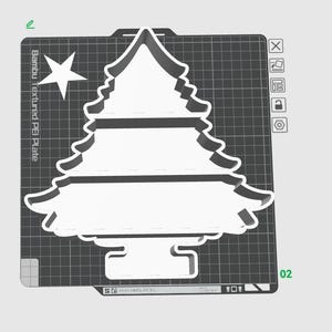 Puede incluir: Un cortador de galletas blanco en forma de árbol de Navidad con una estrella, colocado sobre una placa PEI texturizada. El cortador tiene un diseño detallado, ideal para hornear en Navidad. La placa tiene un patrón de cuadrícula.