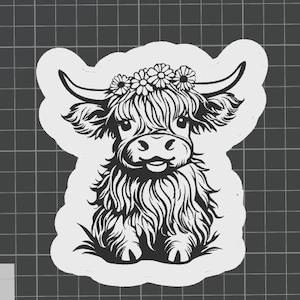 May include: Black and white illustration of a Highland cow with a flower crown. The cow has long, shaggy fur and large horns. The design is a sticker or decal, with a white outline.