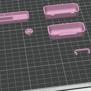 May include: A collection of pink 3D-printed storage containers and accessories. The set includes two rectangular boxes with hinged lids, a small tray with compartments, a circular piece, and a handle. The items are arranged on a grid.