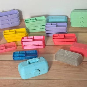May include: A collection of colorful plastic organizers in various shapes and sizes. The organizers are in shades of pink, blue, yellow, green, and purple. Some have compartments, and others are stacked.