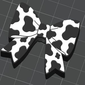 May include: A black and white cow print bow. The bow is a decorative accessory, featuring a repeating pattern of black spots on a white background. The bow is tied in the centre and has a three-dimensional appearance.