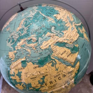 Peut inclure: Un globe vintage aux couleurs turquoise et beige, représentant les continents et les pays. Le globe est monté sur un support métallique et présente des détails géographiques, notamment les noms des pays et des étendues d'eau.