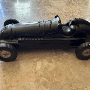 Pode incluir: Um carro de corrida de brinquedo preto vintage com quatro rodas. O carro tem uma carroceria aerodinâmica, um cockpit e um compartimento do motor detalhado. As rodas são pretas com aros prateados. O brinquedo é de plástico.