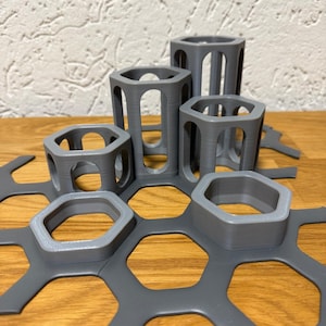 Può includere: Una collezione di supporti e pezzi di collegamento esagonali grigi. I supporti sono aperti sui lati e di altezza variabile. I pezzi di collegamento hanno aperture esagonali. Gli oggetti sono disposti su una superficie di legno.