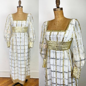 May include: A white maxi dress with gold and silver stripes. The dress has a square neckline, long sleeves, and a fitted bodice. The dress is made of a sheer fabric and has a flowing skirt.
