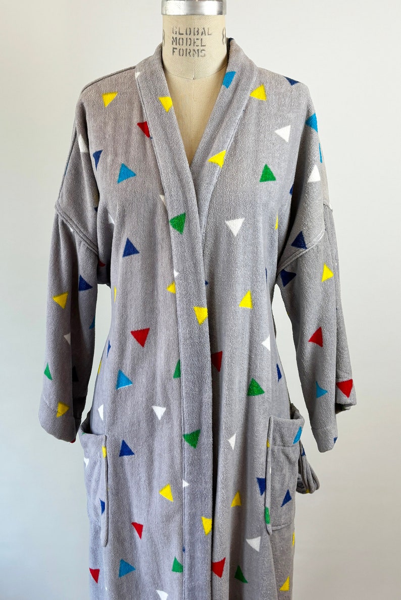 May include: A gray robe with a colorful triangle pattern. The robe has a shawl collar and long sleeves. The robe is made of a soft, comfortable material.
