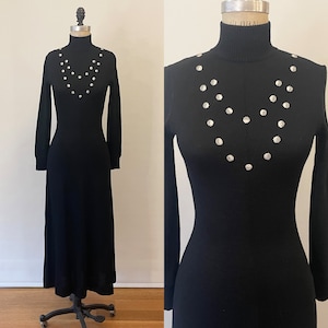 May include: A black long-sleeved turtleneck dress with a silver button detail around the neckline.