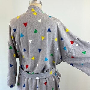 May include: Gray bathrobe with a colorful geometric pattern of triangles. The robe has a tie belt and long sleeves.