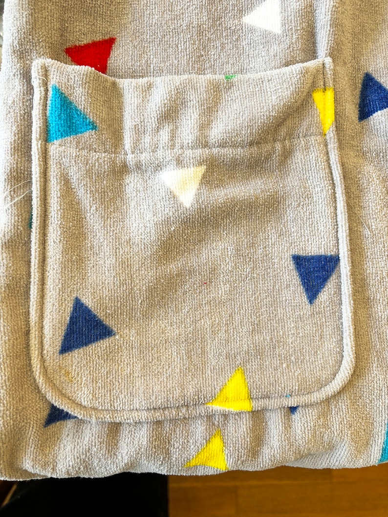 May include: A gray hooded towel with a pocket on the front. The towel has a pattern of colorful triangles.