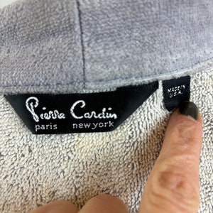 May include: A gray Pierre Cardin label with the text "Pierre Cardin" in black, "paris" in black, and "new york" in black. The label also has a smaller white label with the text "MADE IN U.S.A." in black.