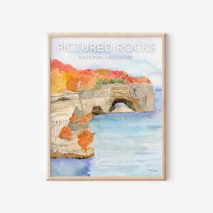 Puede incluir: Pintura acuarela de una formación rocosa con un arco, rodeada de follaje de otoño, con el texto "Pictured Rocks National Lakeshore" sobre la imagen.