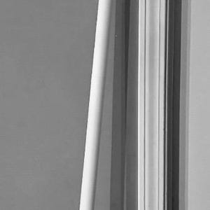 May include: A tall, white staff with a detailed, geometric top design. The staff leans against a wall and door frame, showcasing its length and intricate craftsmanship. The staff appears to be made of wood or a similar material.