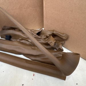 May include: A brown tobacco pipe with a curved stem and bowl, lying on a white surface. Several other brown objects, possibly parts of the pipe or related items, are also visible. Cardboard boxes are in the background.