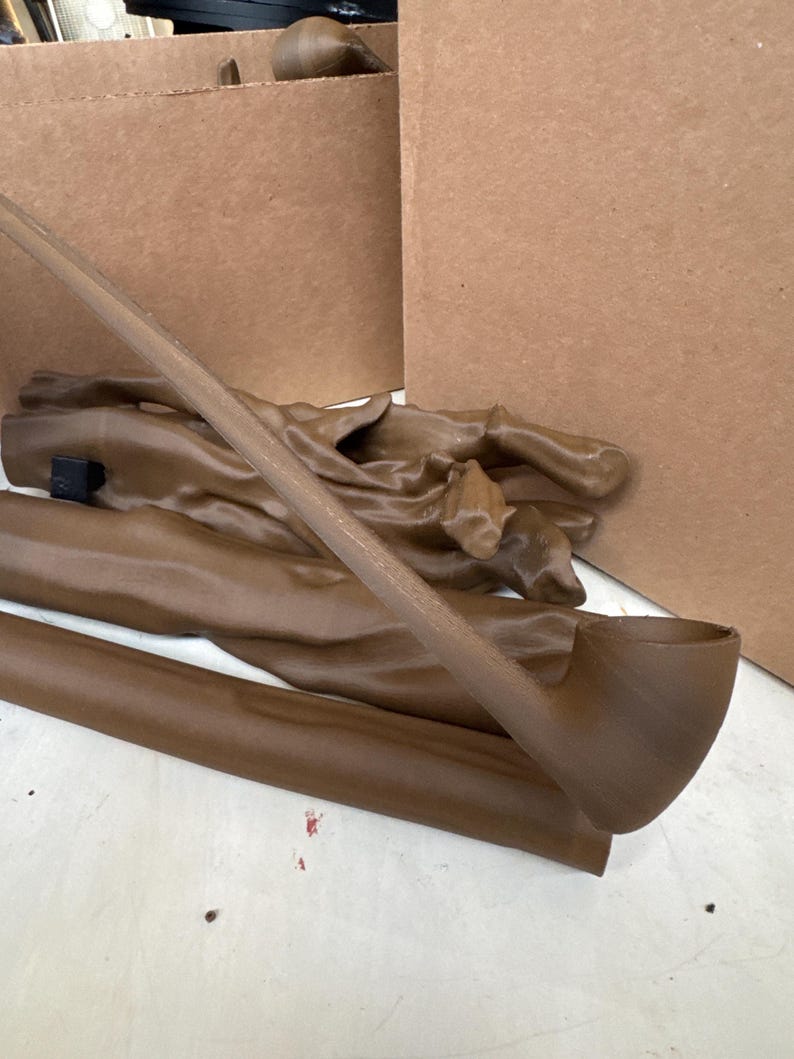 May include: A brown tobacco pipe with a curved stem and bowl, lying on a white surface. Several other brown objects, possibly parts of the pipe or related items, are also visible. Cardboard boxes are in the background.