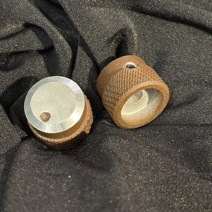 May include: Two round knobs, one is silver with a small hole in the center, the other is brown with a textured surface and a small hole in the center.