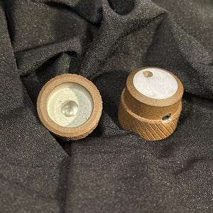 May include: Two brown knobs with a textured surface and a silver center. The knobs have a white circle on the top.