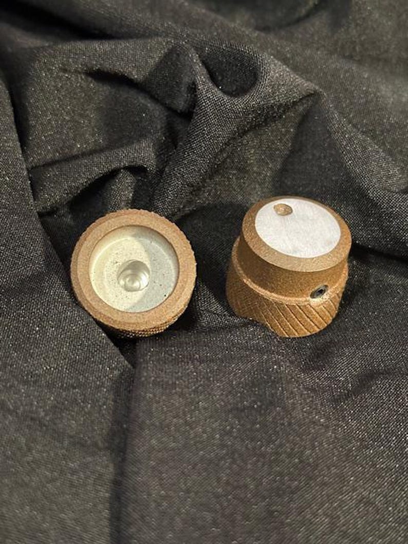 May include: Two brown knobs with a textured surface and a silver center. The knobs have a white circle on the top.