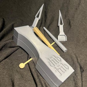 May include: A gray 3D printed box with the words "Club Med" on the side. The box contains a set of tools, including a small wooden stick, a gray metal tool with a pointed end, and a gray metal tool with a flat end.