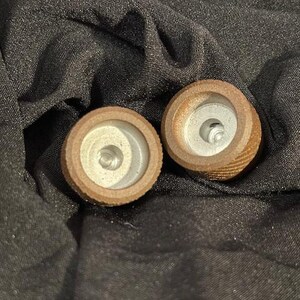 May include: Two wooden tops with a white center and a brown outer ring. The tops have a small hole in the center.