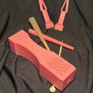 May include: A collection of pink 3D-printed tools, including a large rectangular piece with the text "dub tub" embossed on it, two pointed tools, and a thin, cylindrical tool. A rolled item and a wooden stick are also present.